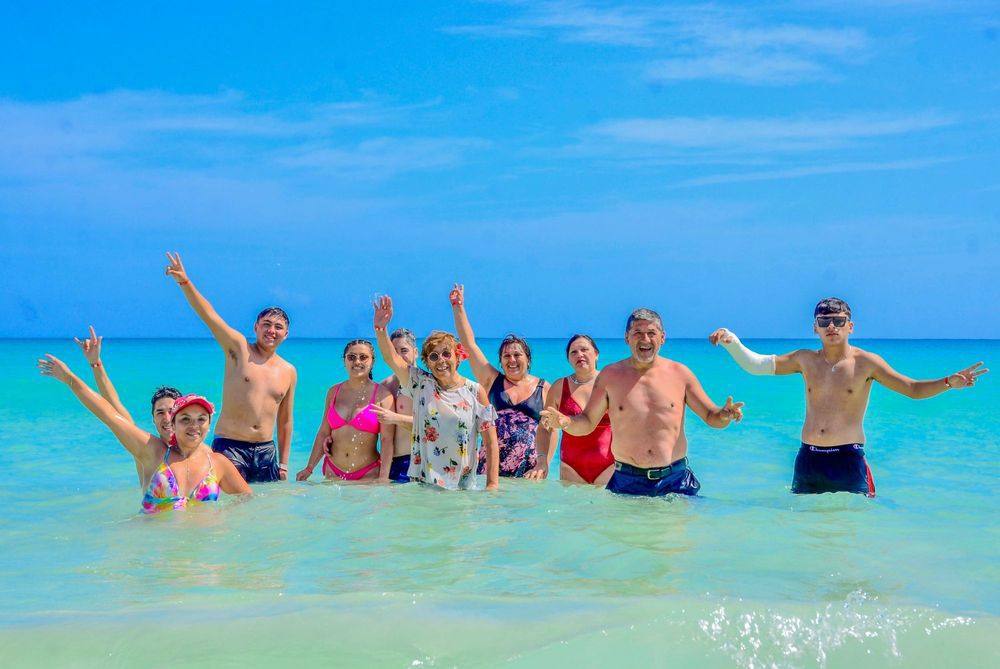 Grupo celebrando con los brazos en alto en el mar turquesa de playa Macao
