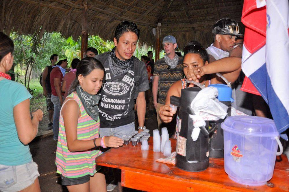Visitantes en una casa típica dominicana con techo de yagua y bandera