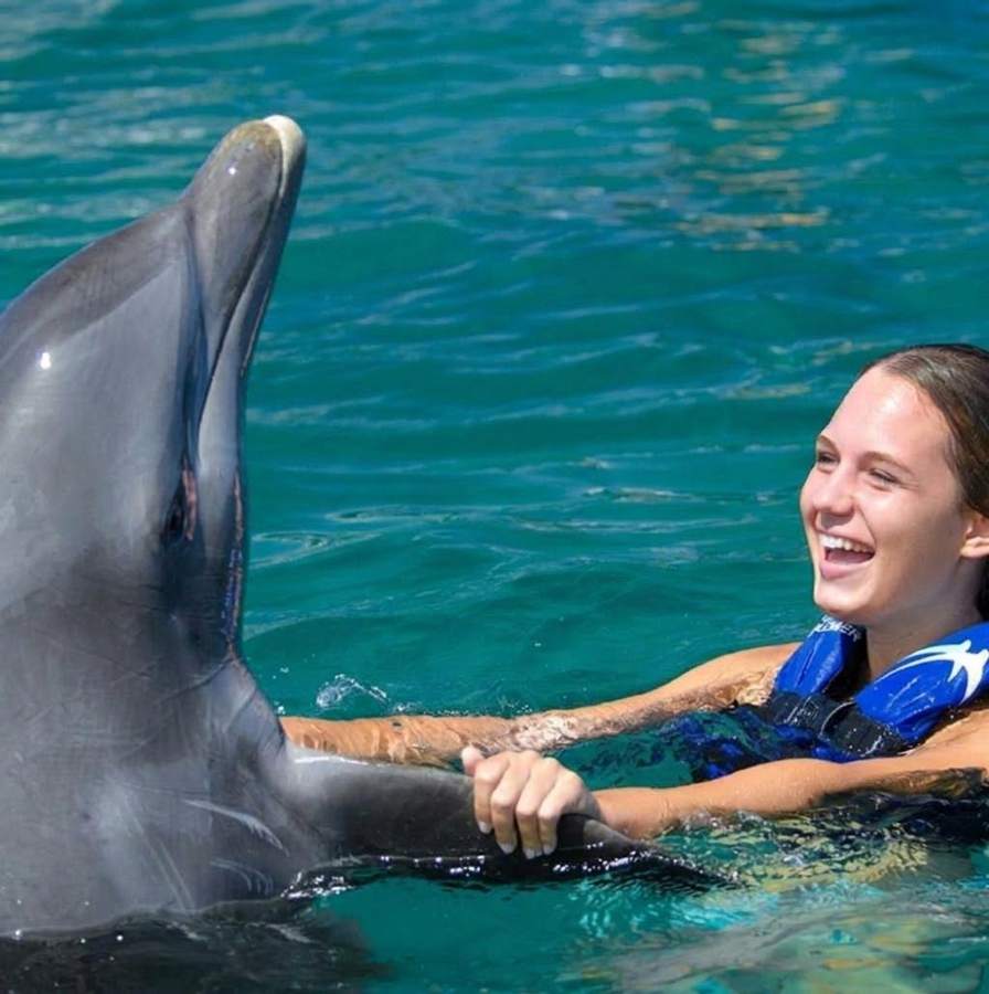 Chica sonriendo junto a un delfín en el agua