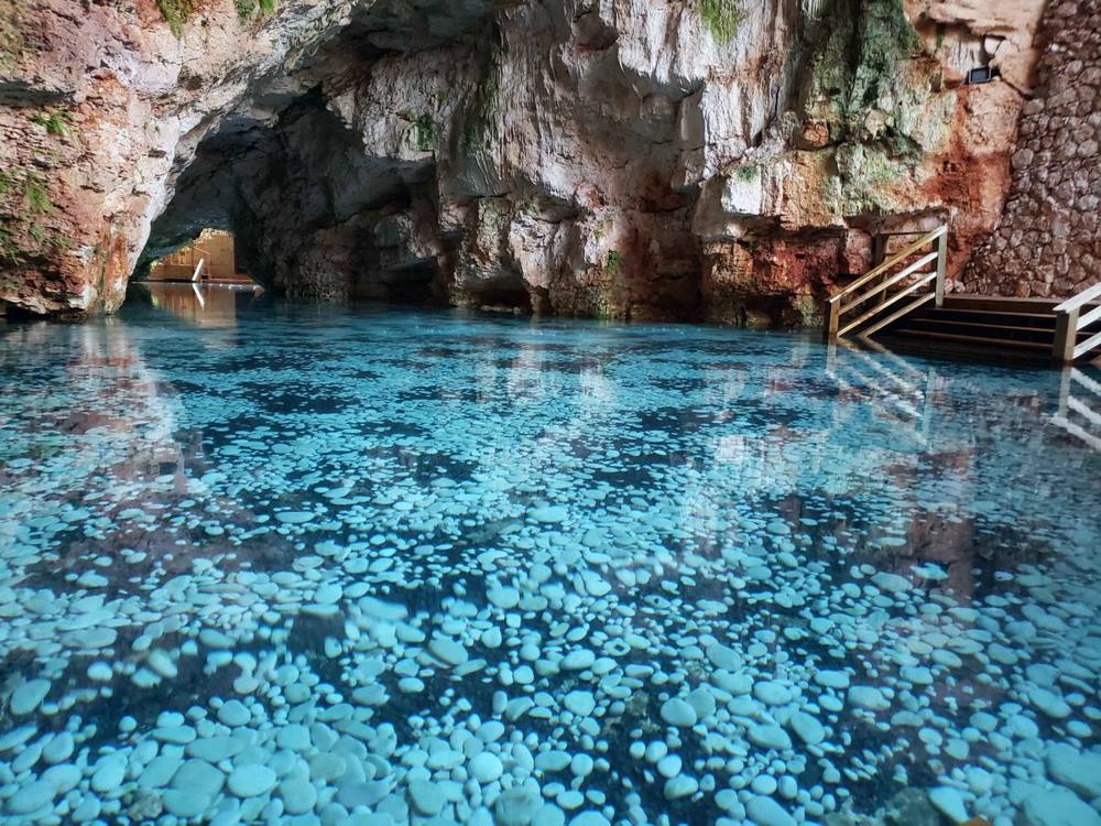 Cenote con aguas turquesa y piedras blancas dentro de la cueva
