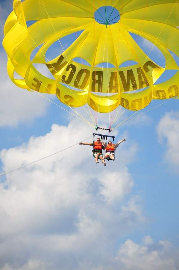 Pareja saludando en pleno vuelo de parasailing
