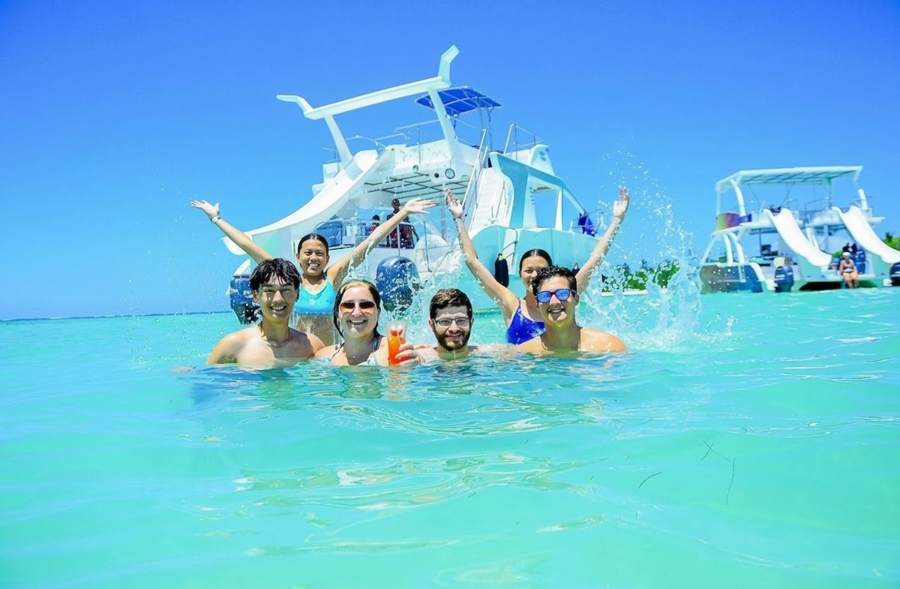 Grupo de amigos en el agua turquesa frente al catamarán del Party Boat en Punta Cana