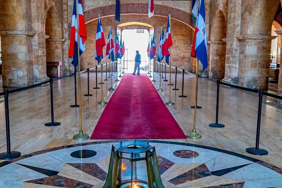 Salón de piedra con banderas dominicanas y llama encendida en el piso de mármol