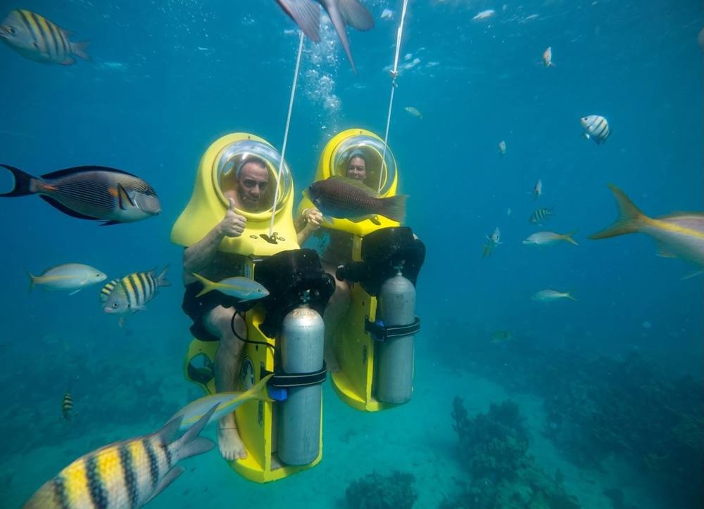 Dos visitantes en scooters submarinos amarillos entre peces en el mar Caribe