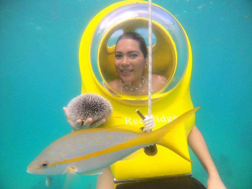 Visitante sonriente dentro de la cúpula del scooter submarino ScubaDoo con un erizo y un pez