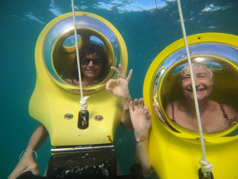 Dos visitantes haciendo la señal de OK bajo el agua en sus scooters submarinos